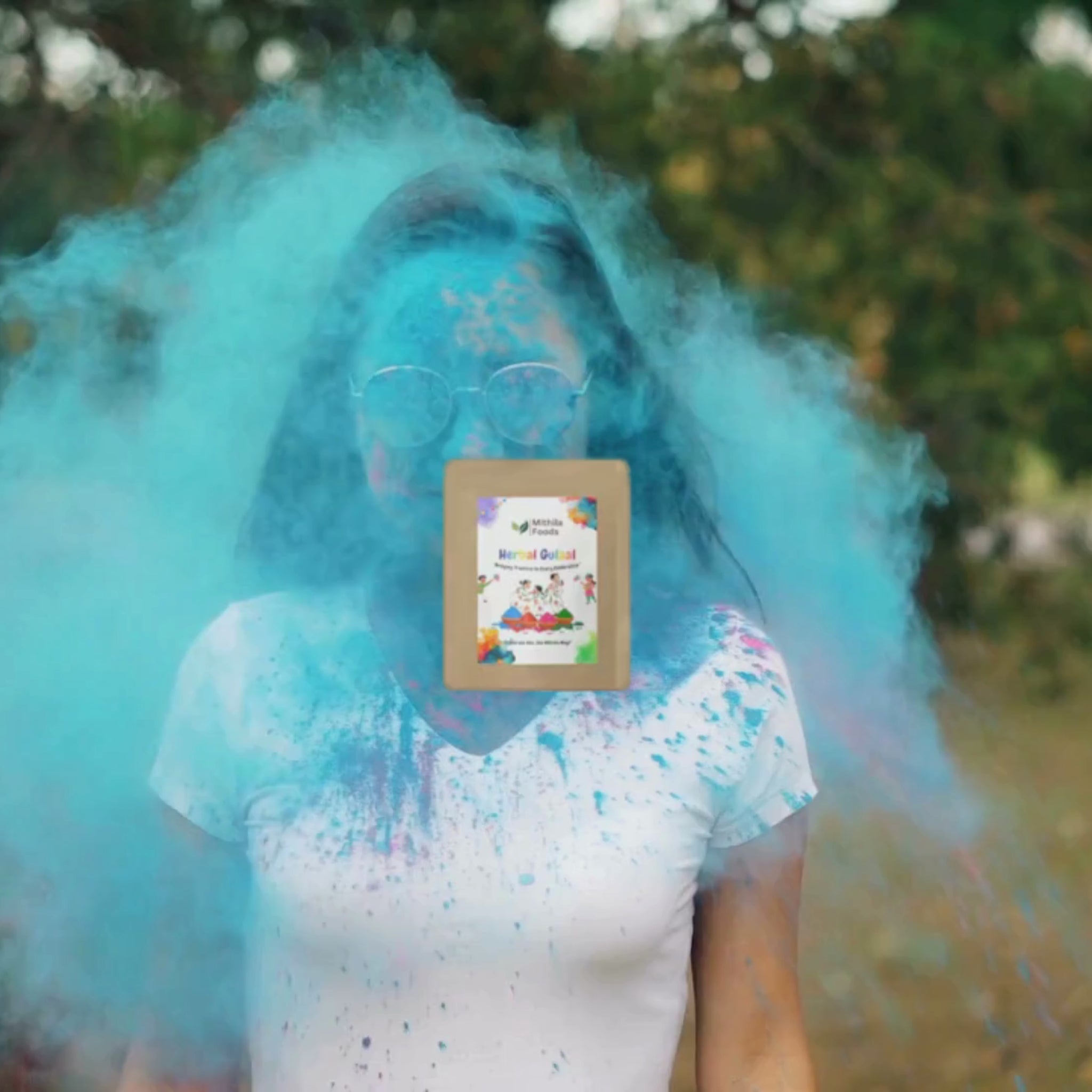  "Mithila Foods Herbal Gulal Holi Colour packs displayed in pink, green, red, purple, and yellow, with group of people playing Holi outdoors in festive mood"